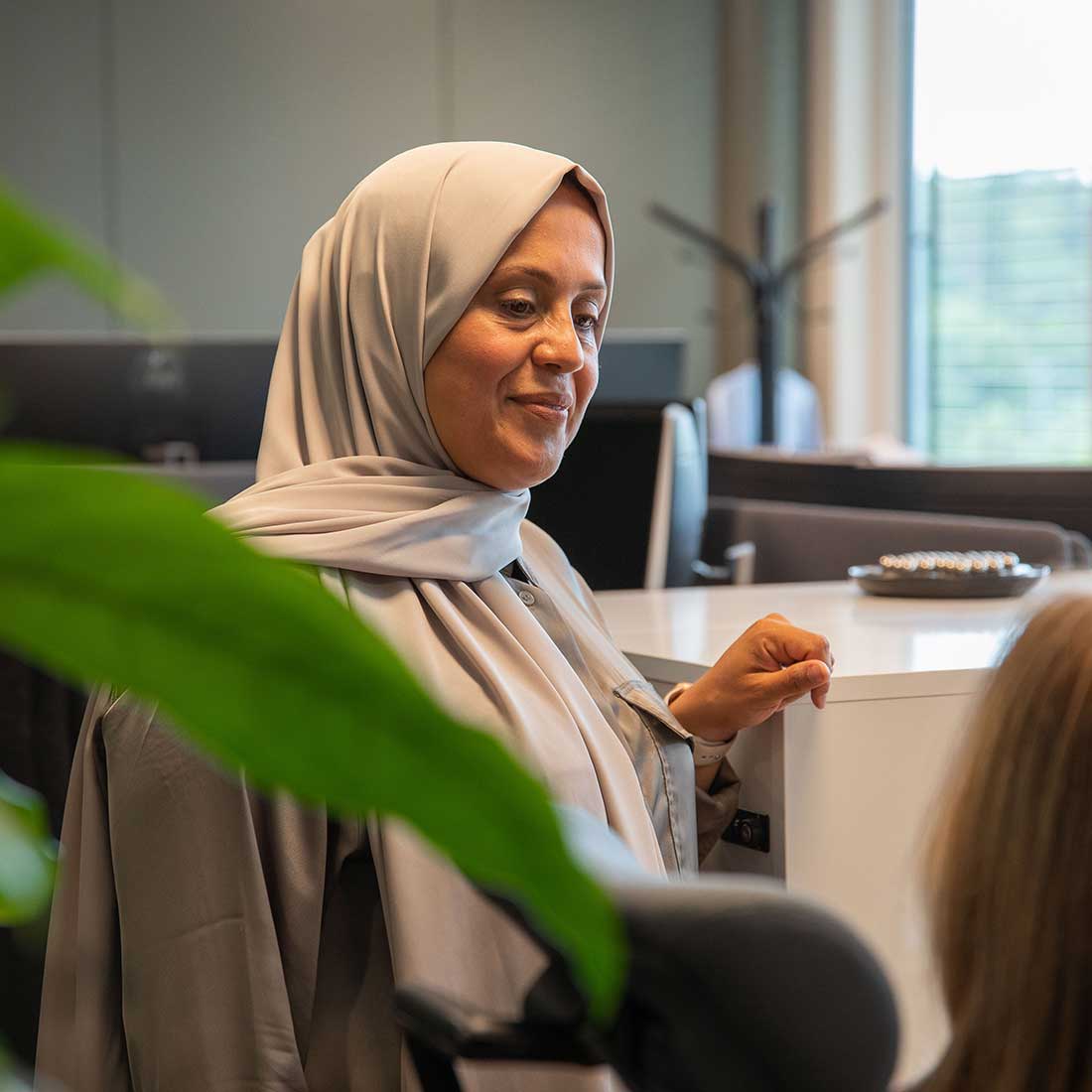 Muslimsk kvinne kledd i hijab i samtale med kollega i kontorlandskap.